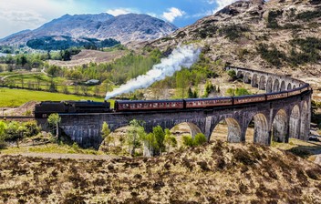Glenfinnan Railway Viaduct in Scotland with the Jacobite steam train against sunset over lake