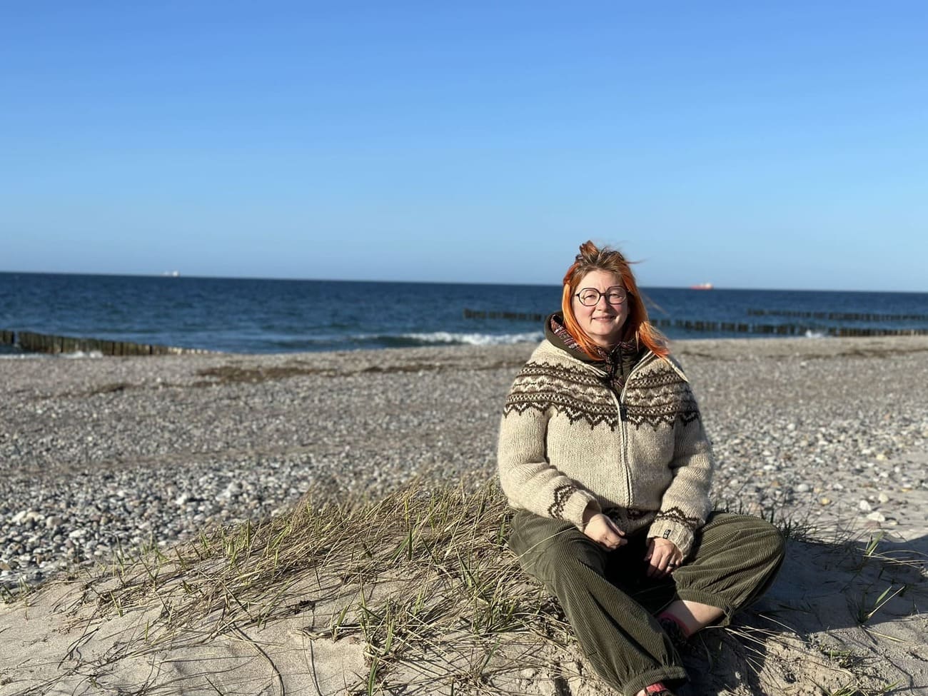 Andrea sitzen, hinter ihr das Meer und blauer Himmel, sie sieht sehr glücklich aus