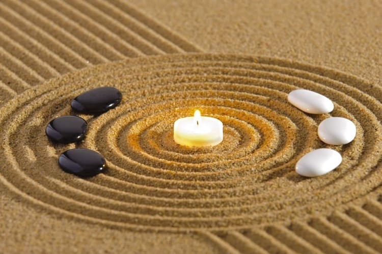 Kreise im Sand und links schwarze Steinen, recht weiße Steinen, in der Mitte einen Kerzen, 