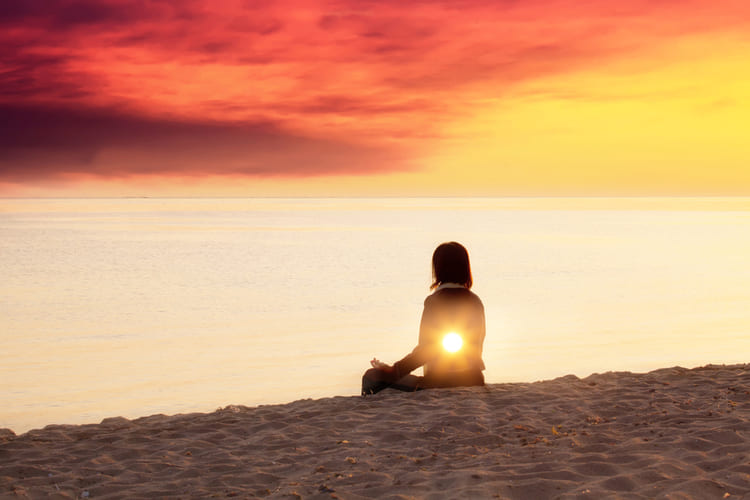 Frau sitzt und schaut auf den Sonnenuntergang, denkt nach, meditiert, selbstzweifel überwinden