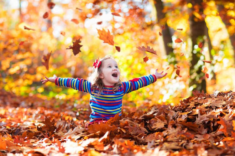 Fröhliches Kind, das im Herbstlaub spielt, symbolisiert den Einfluss von Naturerlebnissen im Vergleich zur Mediennutzung auf das Leben von Kindern.