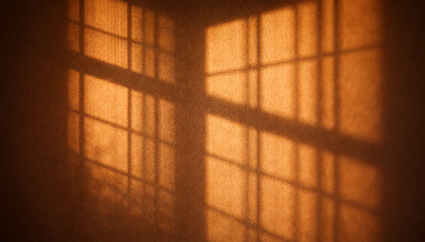 glaubensaetze-erkennen Warmes Licht wirft Fensterschatten an eine Wand – Sinnbild für unbewusste innere Muster und Glaubenssätze.