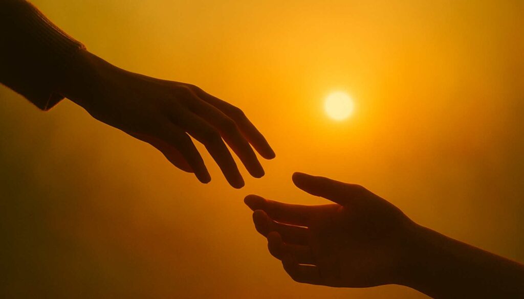 Zwei Hände nähern sich im goldenen Licht der Sonne, ihre Fingerspitzen fast berührend – Symbol für bewusste Nähe und energetische Balance